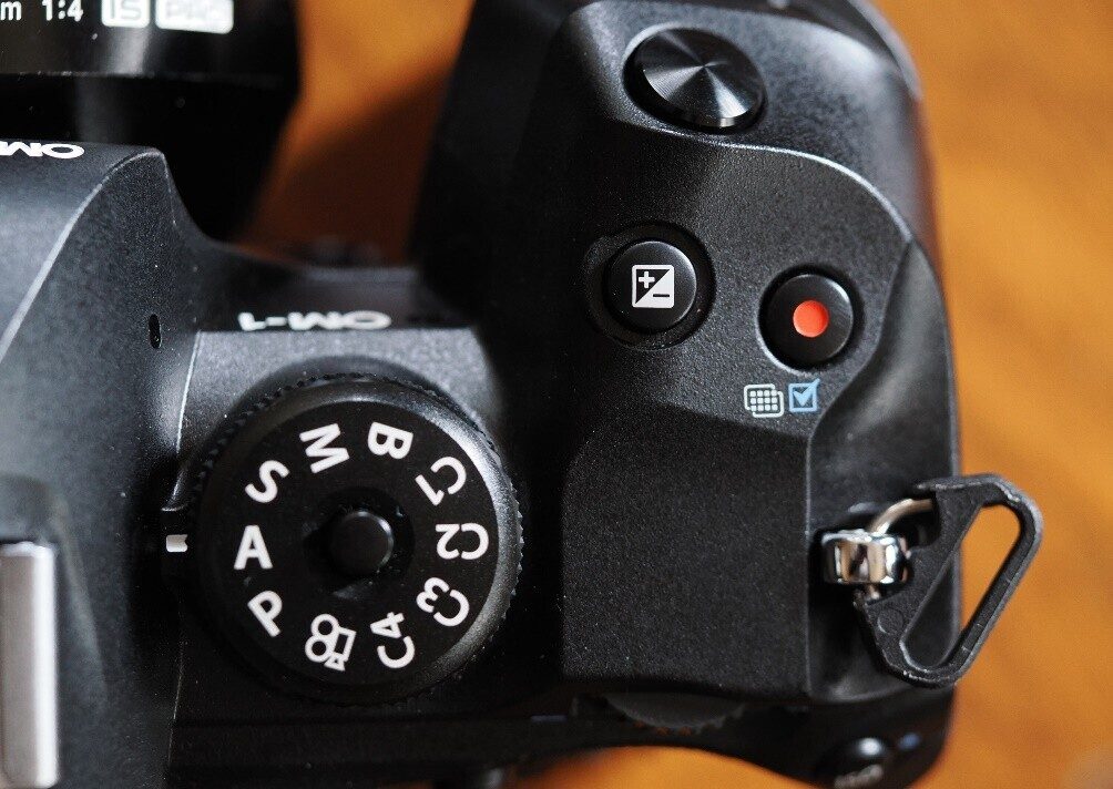 The mode dial and exposure compensation button on an OM-1 camera